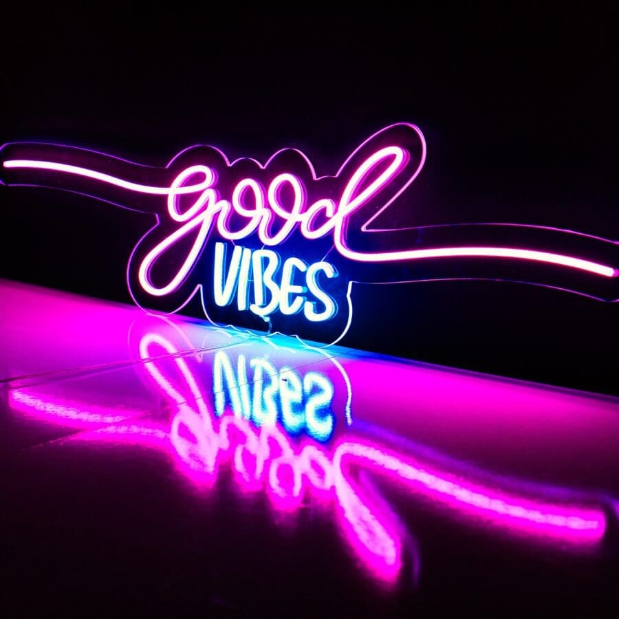 Neón Good Vibes que muestra las palabras "buenas vibraciones" con un reflejo en una superficie brillante.