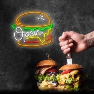 Una persona cortando una hamburguesa con un cuchillo frente a un cartel de Neón Open Burger. #AmorDeHamburguesa