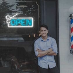 Un hombre parado frente a una barbería con un cartel de "Neón Open Peluquería" iluminado por una luz de neón.