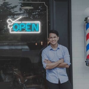 Un hombre parado frente a una barbería con un cartel de "Neón Open Peluquería" iluminado por una luz de neón.