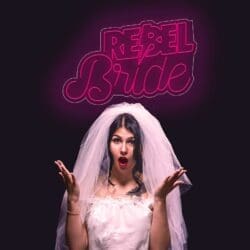 Una mujer con un vestido de novia sosteniendo un cartel que dice "Neón Rebel Bride" con un tema de neón.