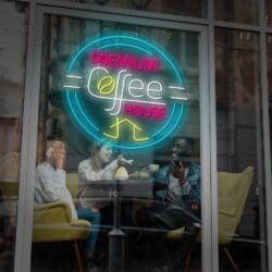 Tres personas riendo y charlando en un Neón Coffe House Premium detrás de un letrero de neón que dice "Neón Coffe con Taza".