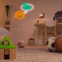 Habitación de un niño con juguetes esparcidos por la alfombra, entre ellos una casa de juguete, una pelota de baloncesto y una pelota de fútbol. Encima, un letrero de neón con la cara de un niño y un globo de diálogo con forma de dinosaurio decoran la pared.