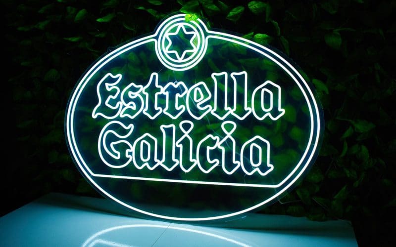 Señal de neón de cerveza estrella galicia sobre un fondo de hojas verdes.